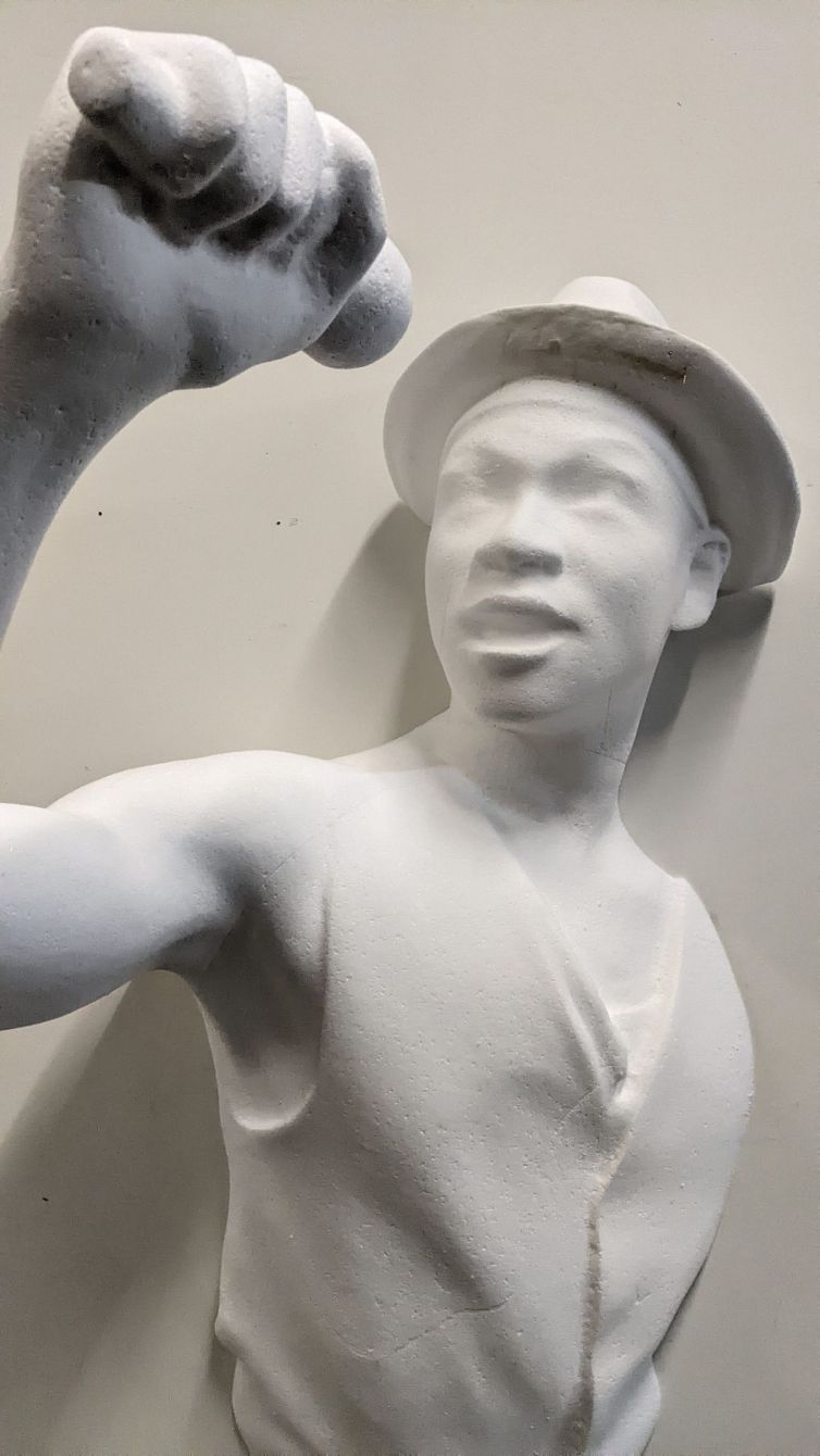 Carved white foam sculpture of man in vest and hat holding microphone