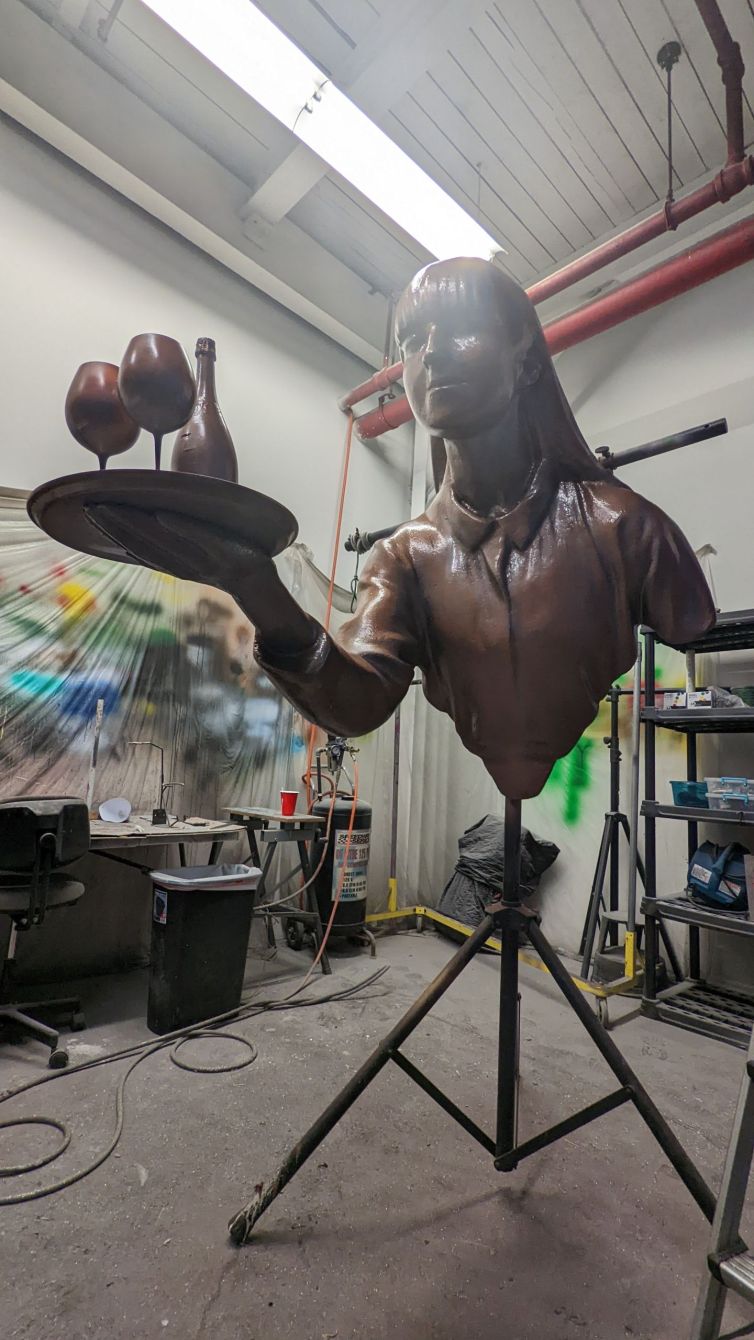 Bronze statue of waitress holding tray of wine and glasses