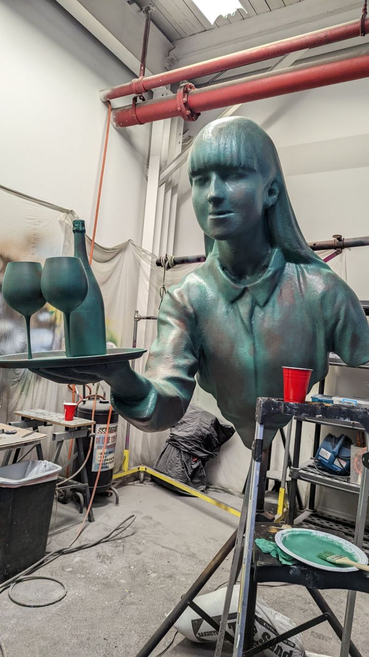 Aged and patinated bronze statue of waitress holding tray of wine and glasses