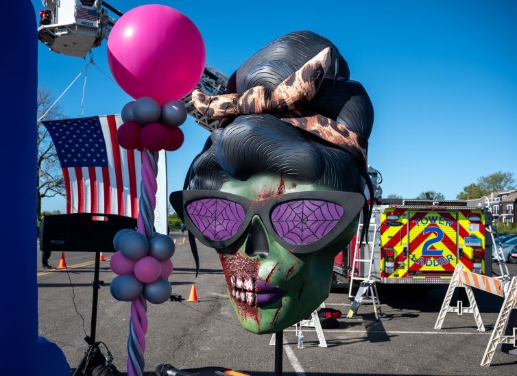 Custom MOMbie female zombie head with beehive hairdo, purple spider web glasses, purple lips, blood splatter, and torn cheek with exposed teeth set up at MOMbies Mother's day charity 5k