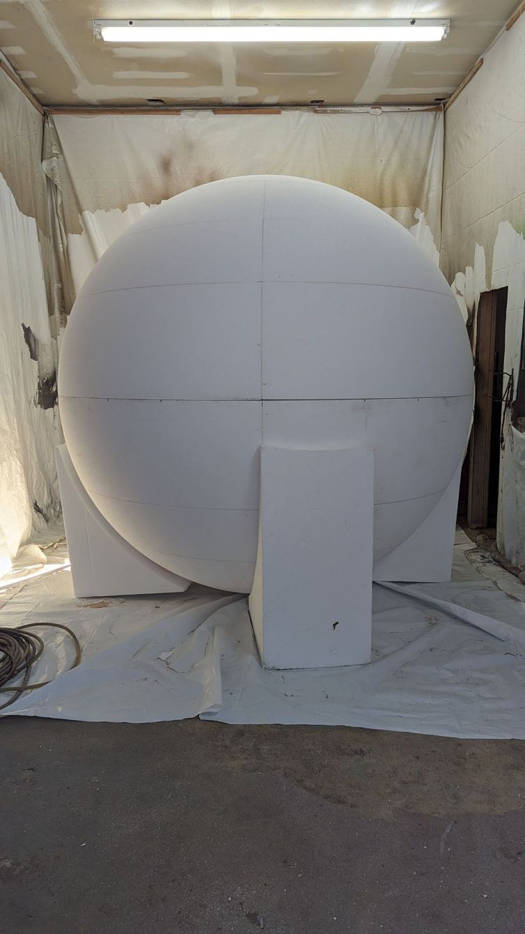 Alignment and hard-coat prep of giant foam ball in paint room with wedge supports to hold in place