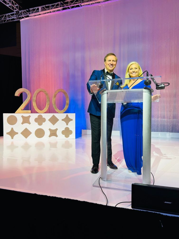 Event hosts Dennis House and Kara Sundlun in front of golden 200 photo-op display